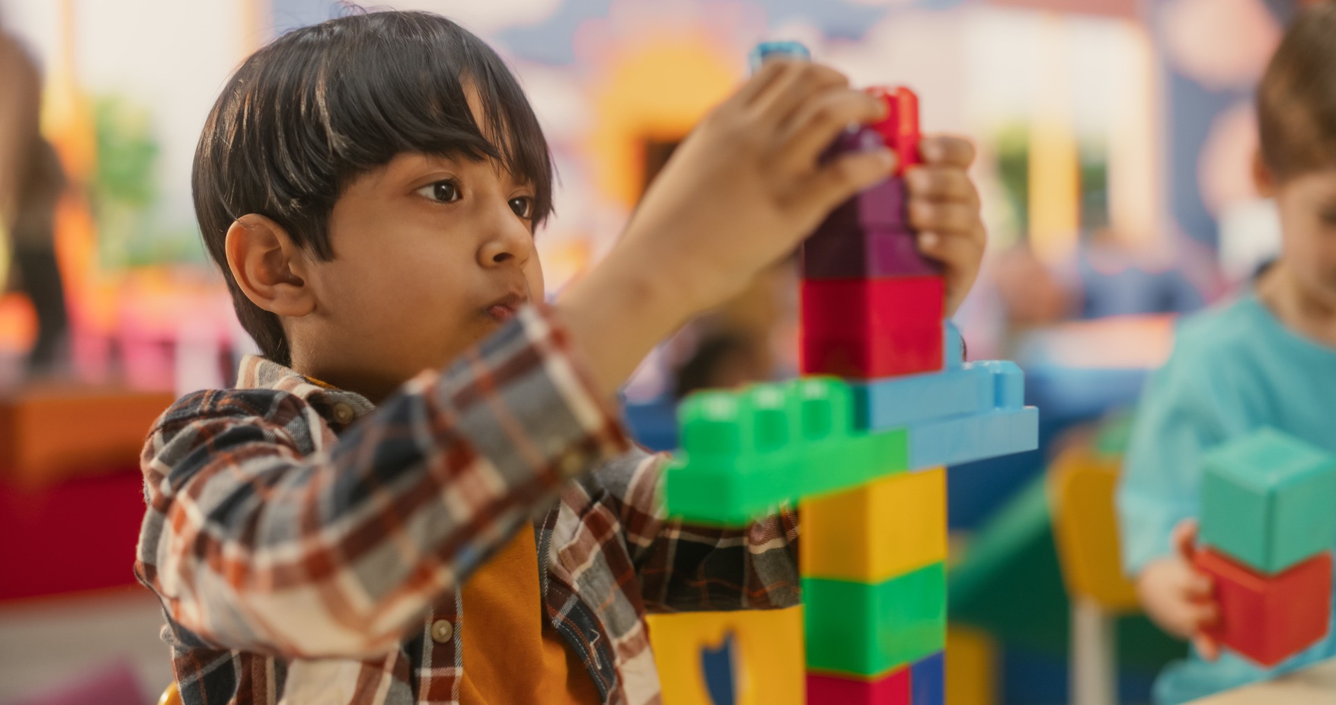 Cute Indian Boy Constructing a Toy Tower Out of Building Blocks. Caucasian Boy and African Girl Playing Together with Colorful Plastic Bricks. Smart Adorable Children Spend Time in Kindergarten